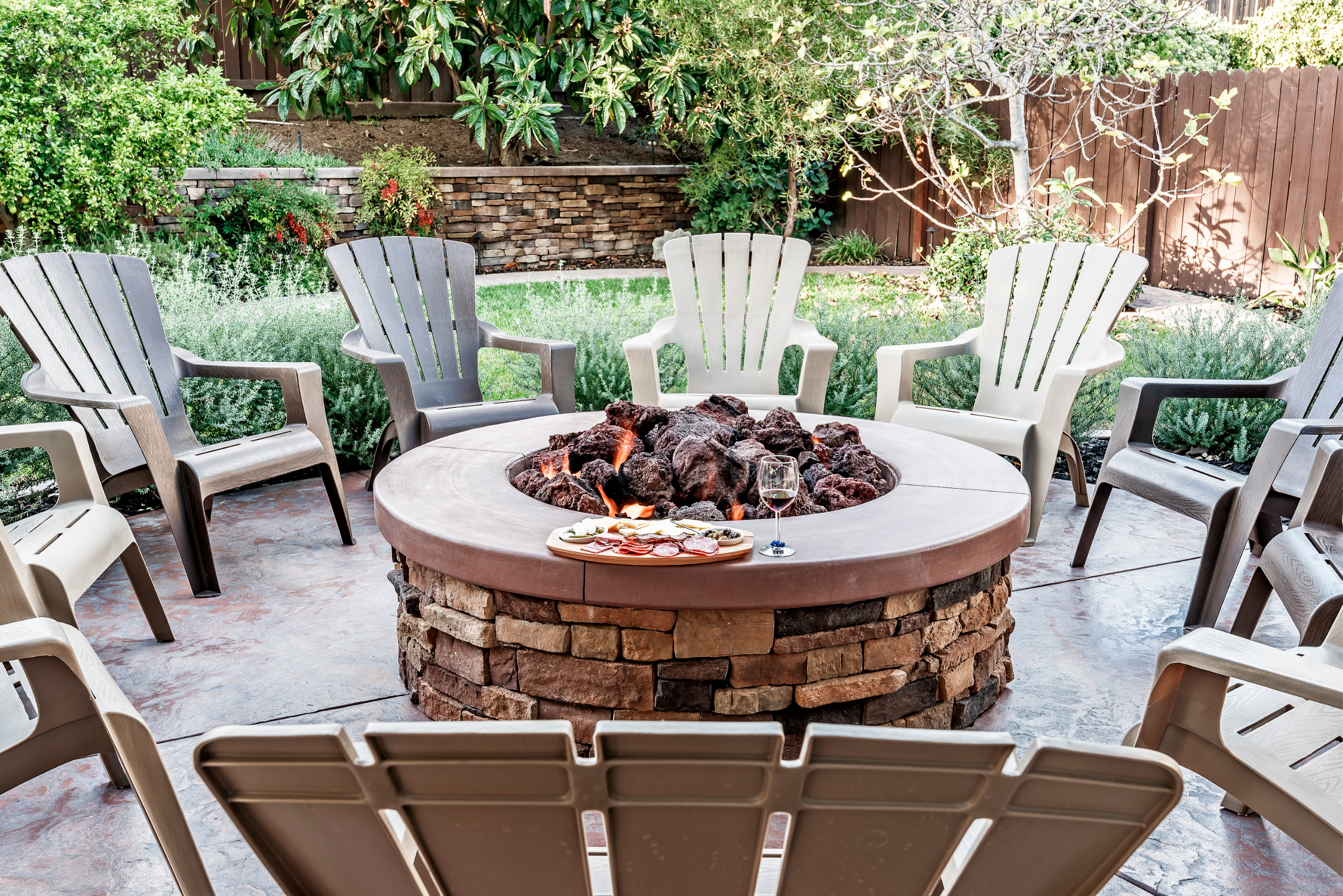 Backyard patio with chairs around a round firepit.
