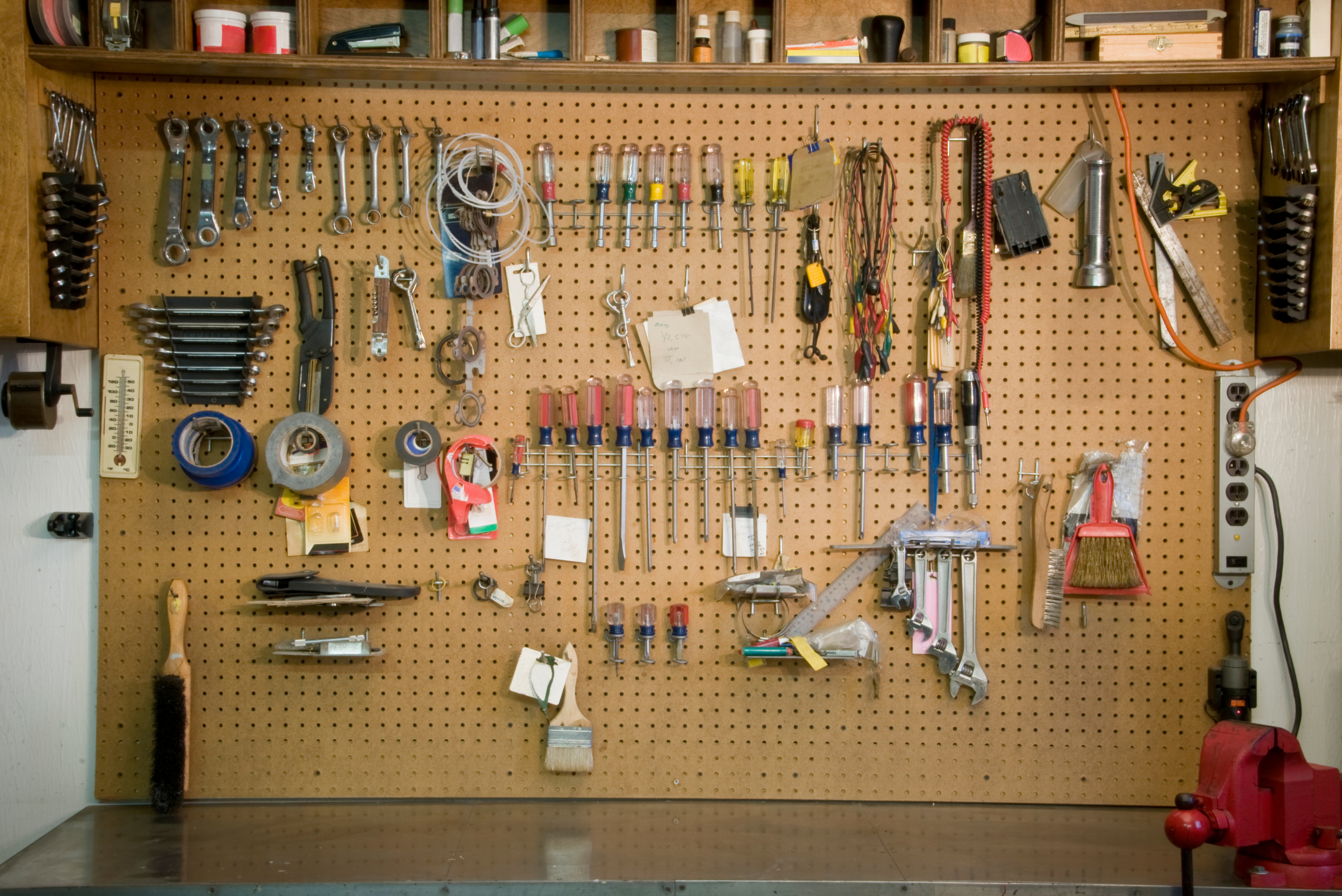 Pegboard with an assortment of tools and a shelf up top.
