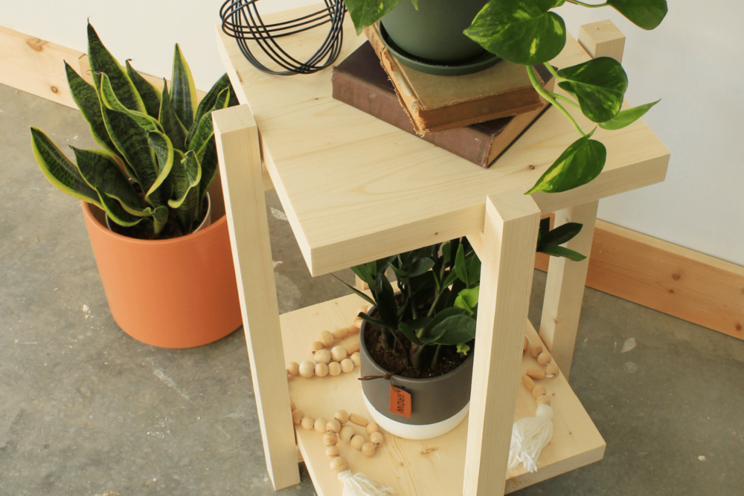 Unfinished wooden plant stand with two levels holding potted plants.