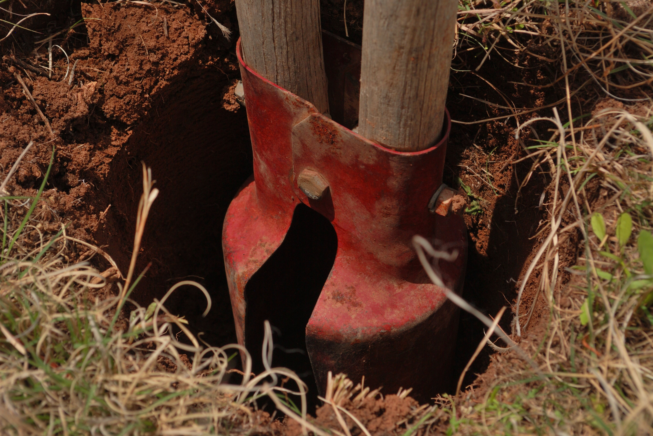 Manual post hole digger with red buckets and wooden handles.