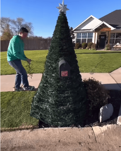 Man wrapping lights around the garland on the mailbox.