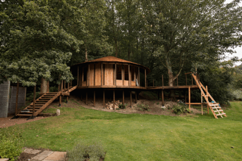 Treehouse that is finished surrounded by grass and walkup stairs.