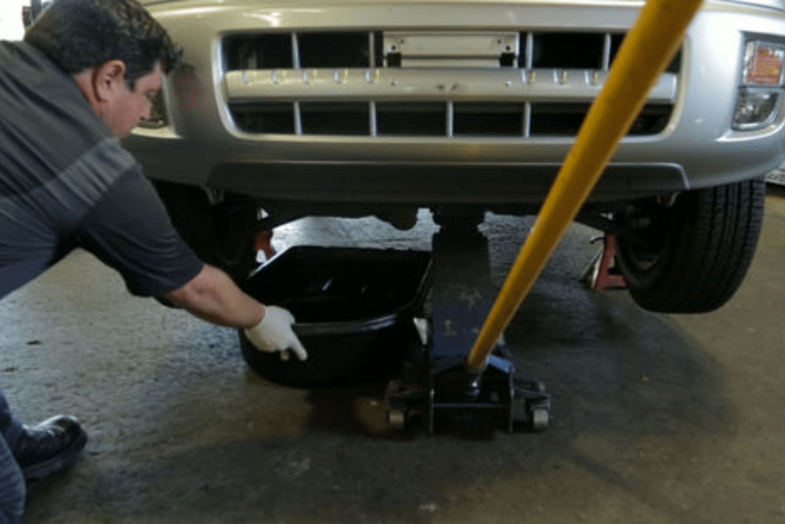 Person pulling out oil catch pan from under a car.