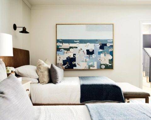 A large beach painting hangs in a welcoming shared cottage bedroom.