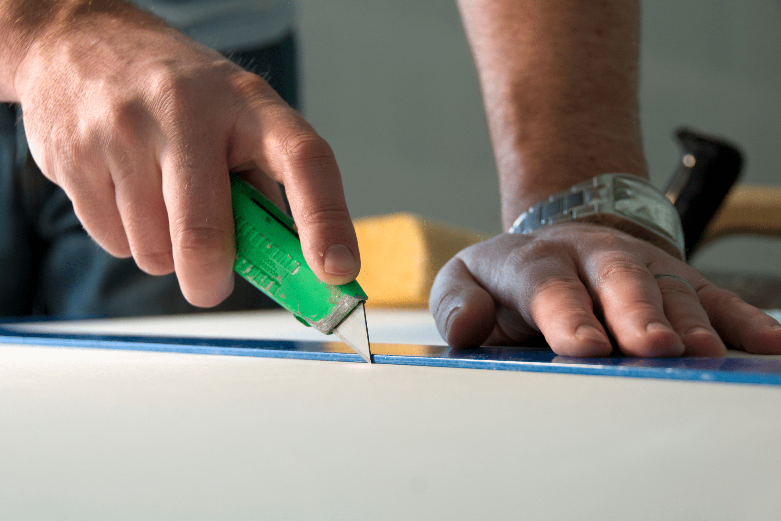 Close up of someone's hands using a utility knife and ruler to cut drywall.