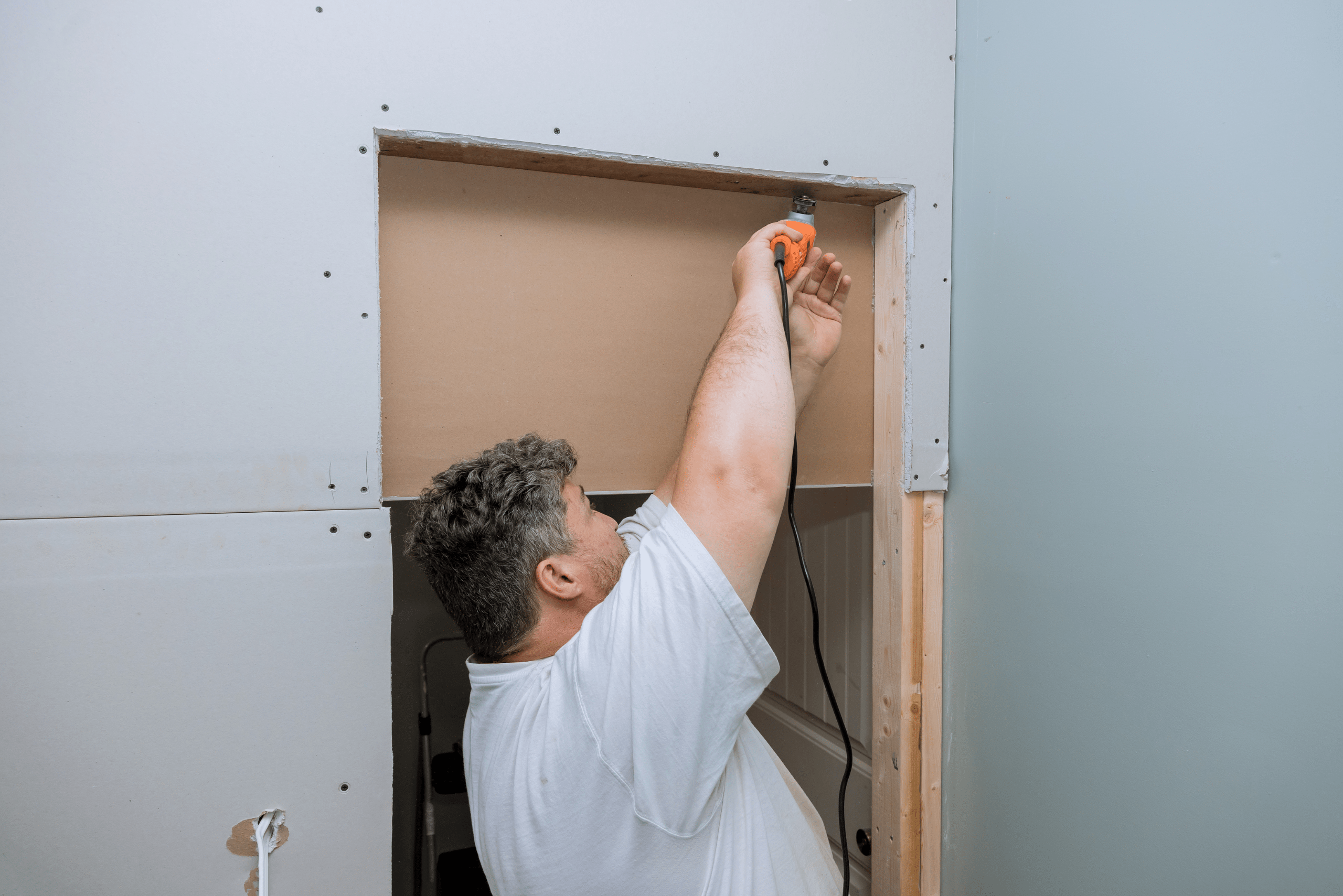 Person wearing a white t-shirt is using an oscillating tool to cut drywall.