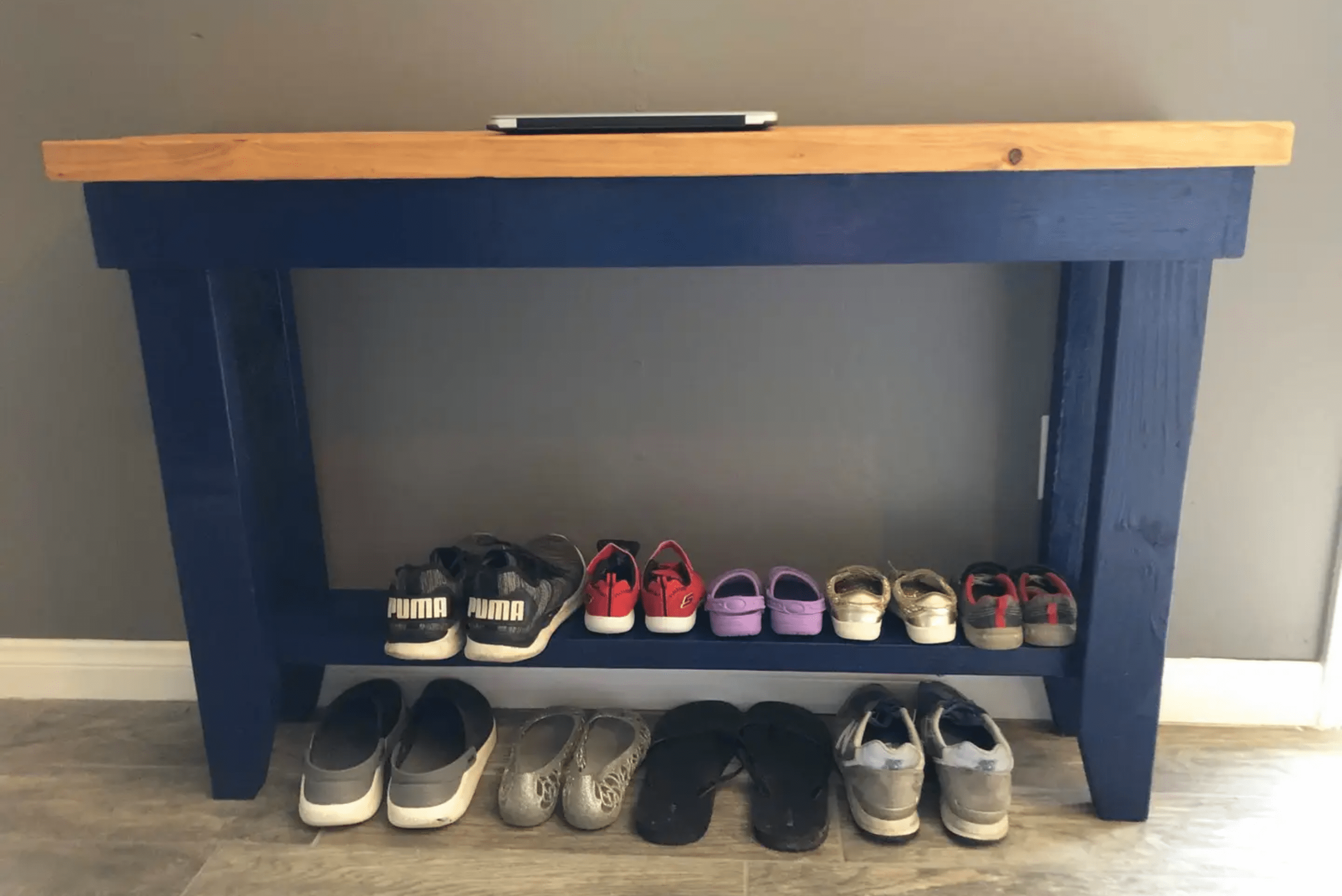 A wooden DIY shoe rack with blue frame and natural wood top that doubles as a bench.