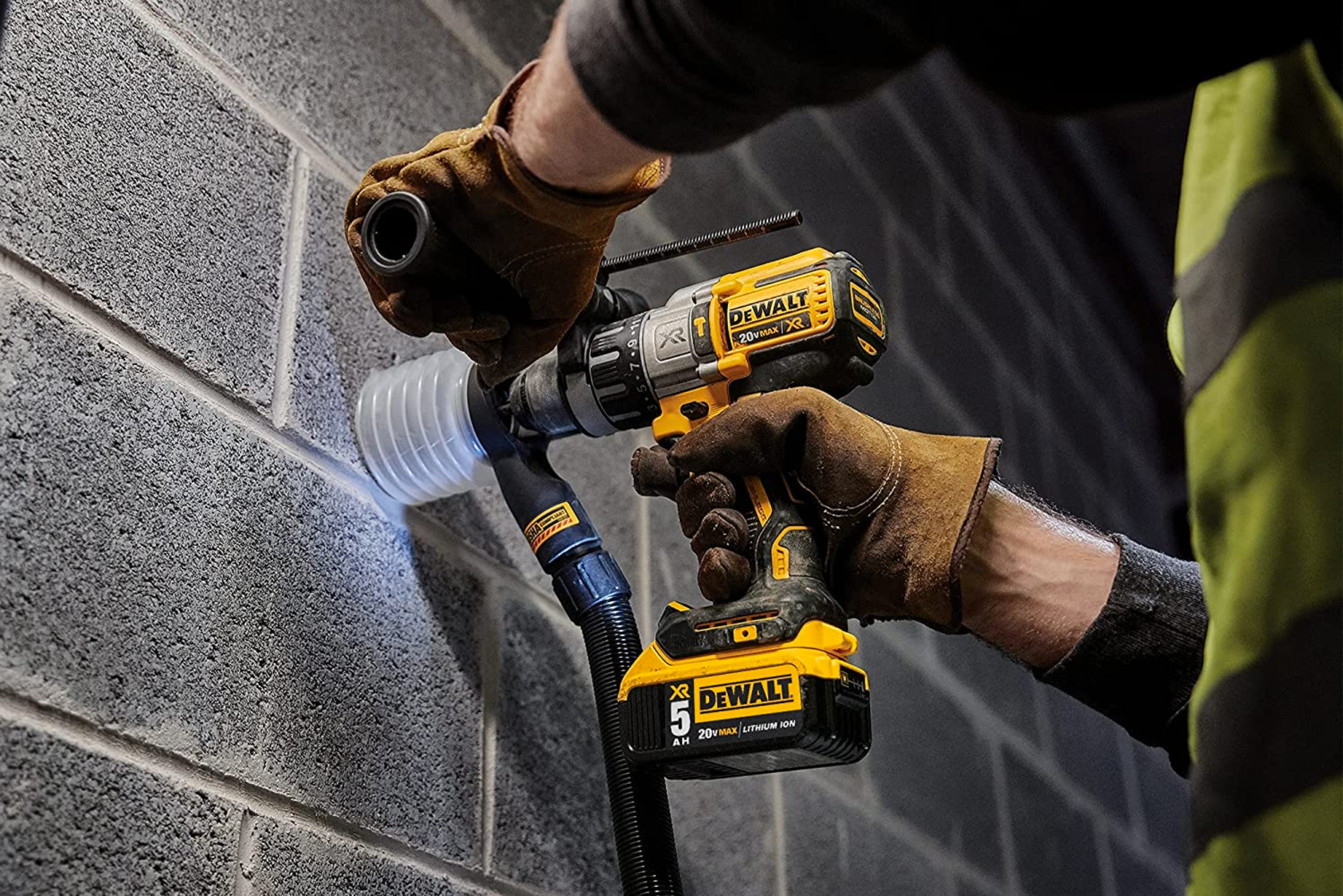 A person using a DeWalt hammer drill on a concrete wall using a dust attachment.