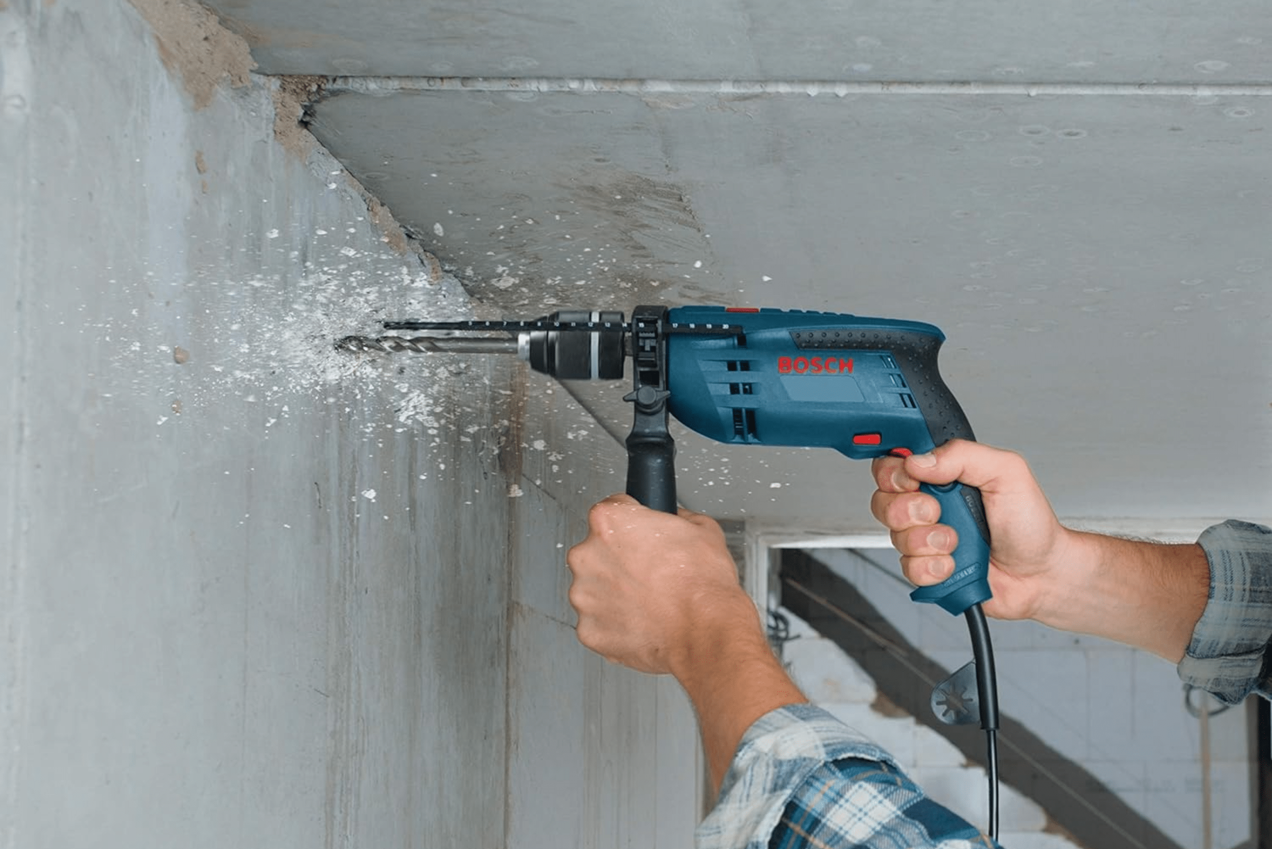 Person using a Bosch hammer drill on a concrete wall.