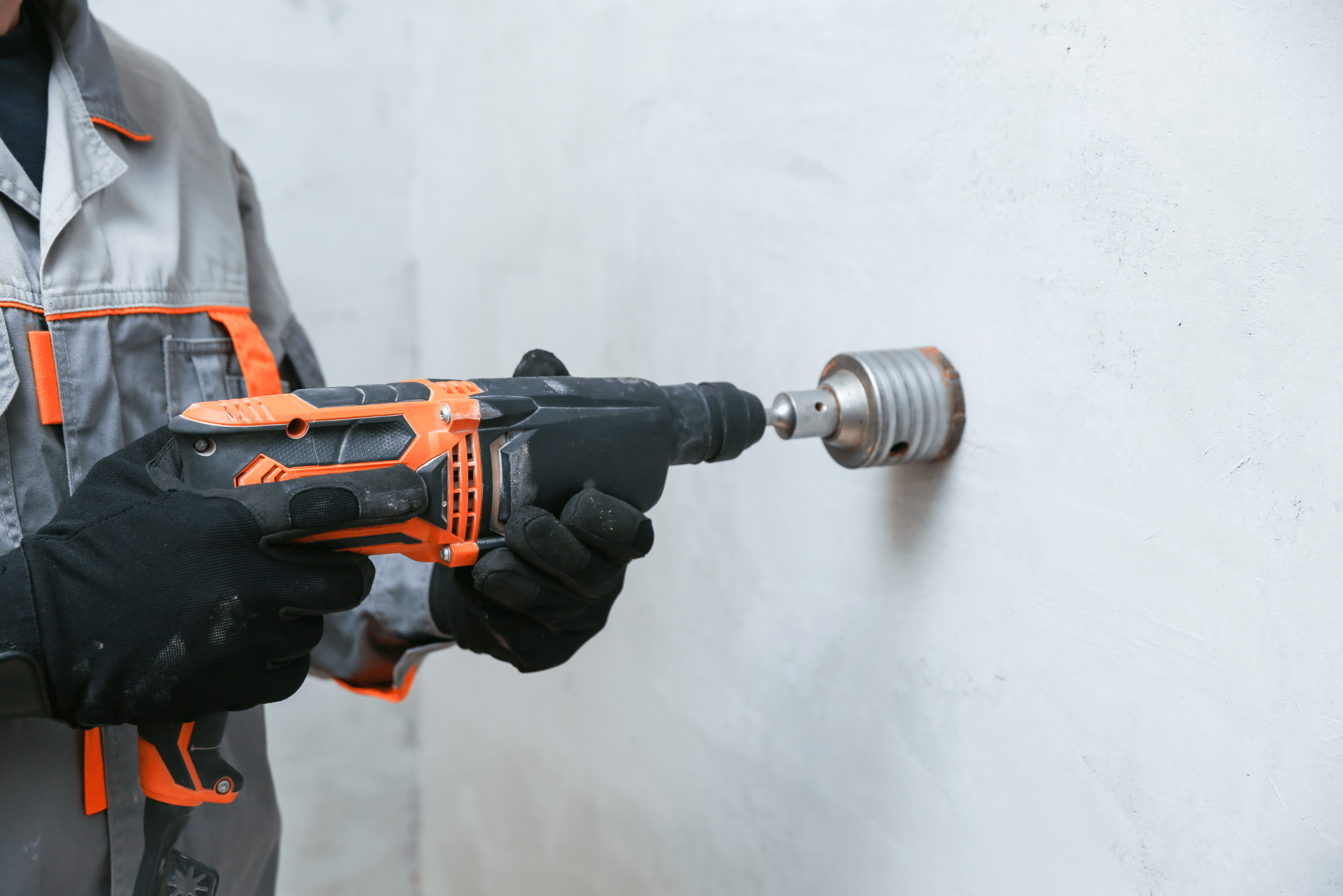 A hammer drill with circular hole bit attachment cutting a hole into the wall.