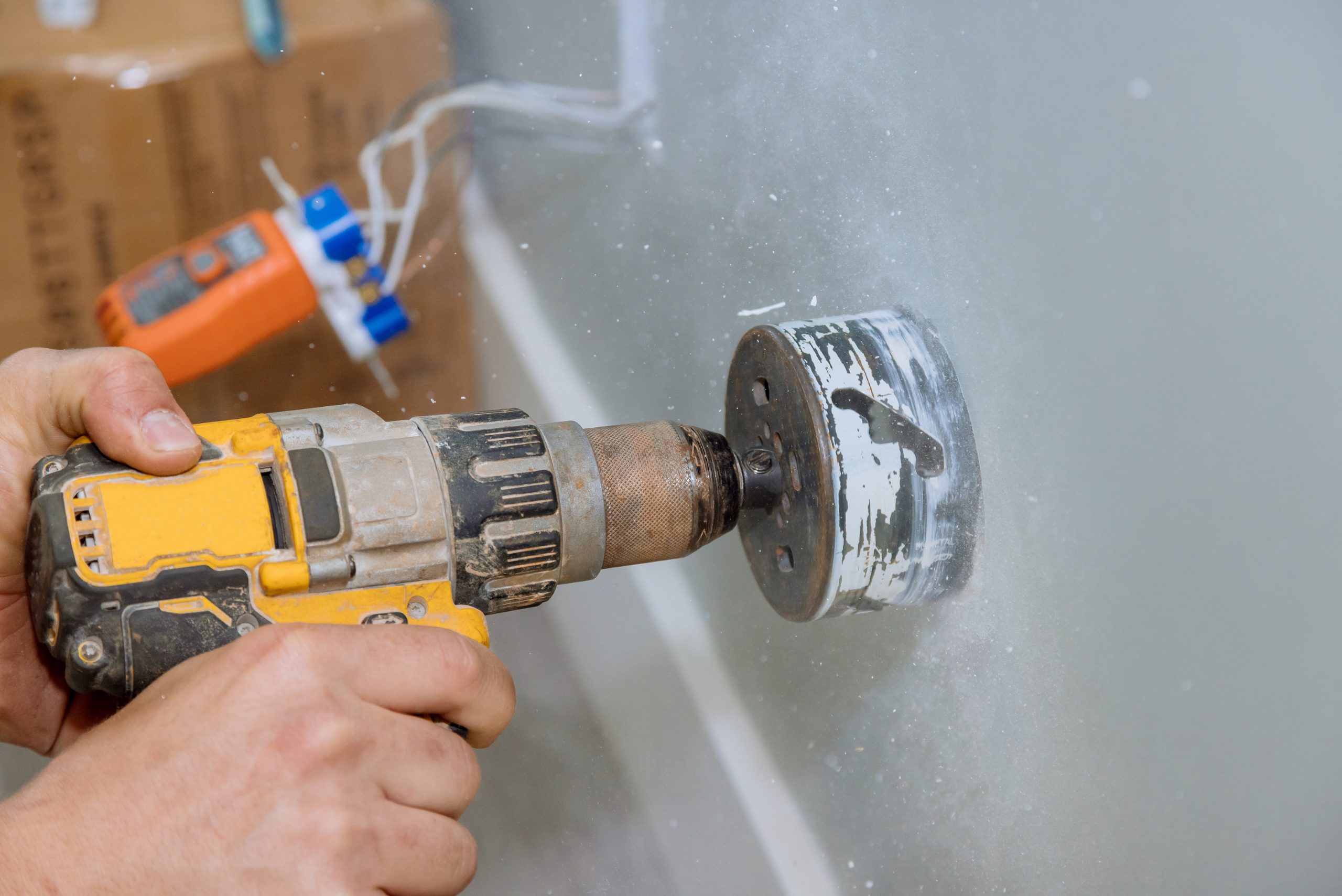 Closeup of hands using a yellow DeWalt drill with hole saw attachment.