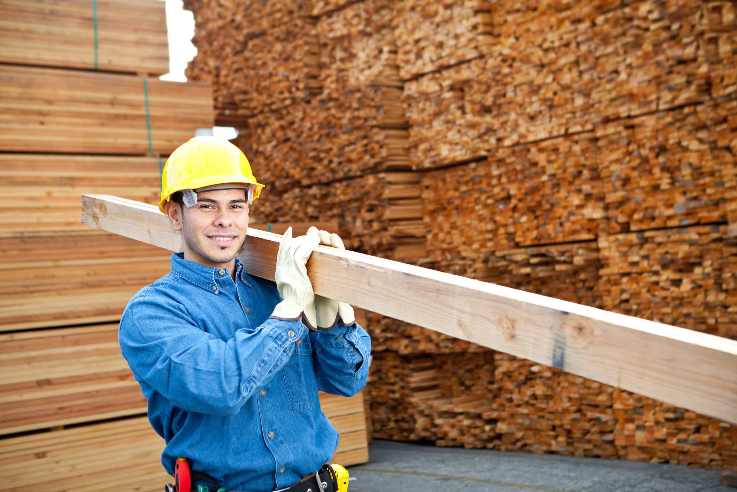 Person carrying a 2x4 piece of wood flanked by a huge wood pile.