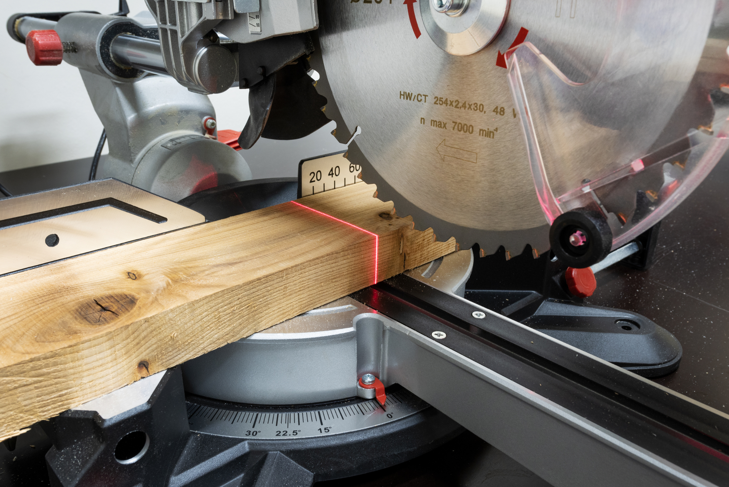 Miter saw blade closeup with a red laser on wood board.