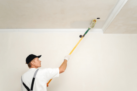 Painter using an extended rod with paint roller to paint the ceiling.