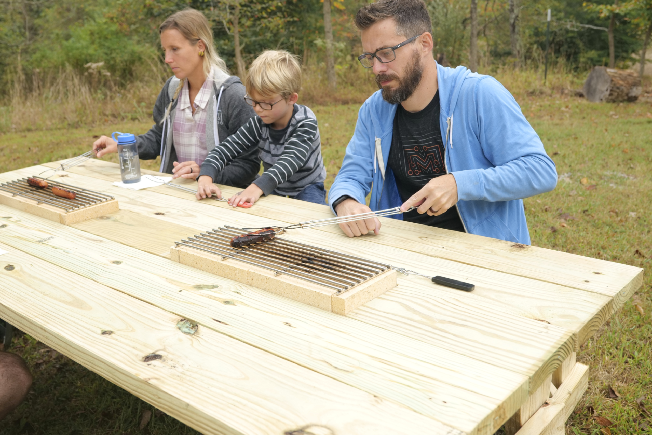Family sitting on a picnic table with built-in grill in the middle.