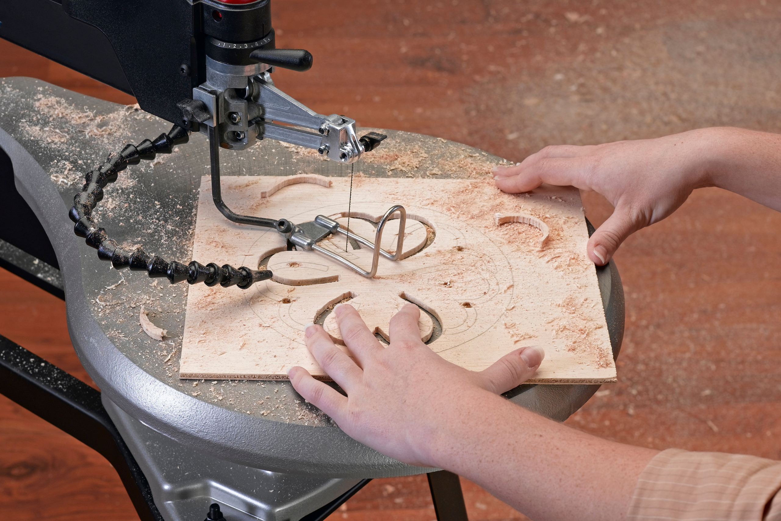 Person's hands guiding wood through a scroll saw to create intricate designs.