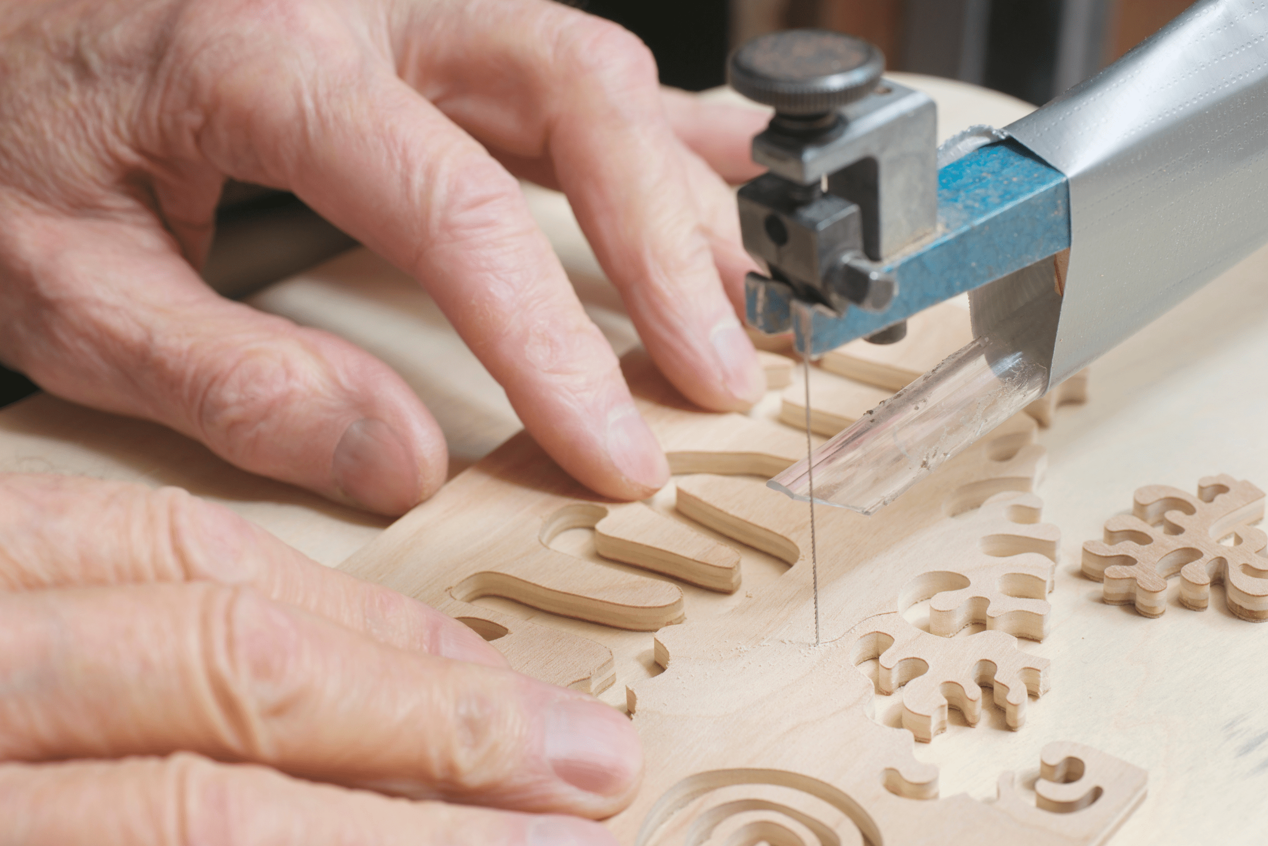 Person's hands cutting small 3D shapes out of wood.