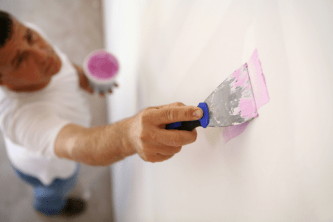 Blurred out man applying pink splatter to repair small damage on drywall.