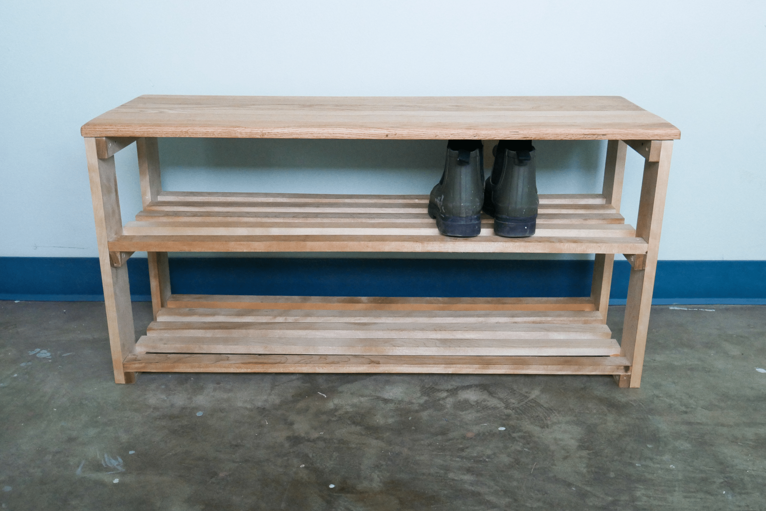 Unfinished DIY wooden shoe rack with one pair of shoes on the second shelf.