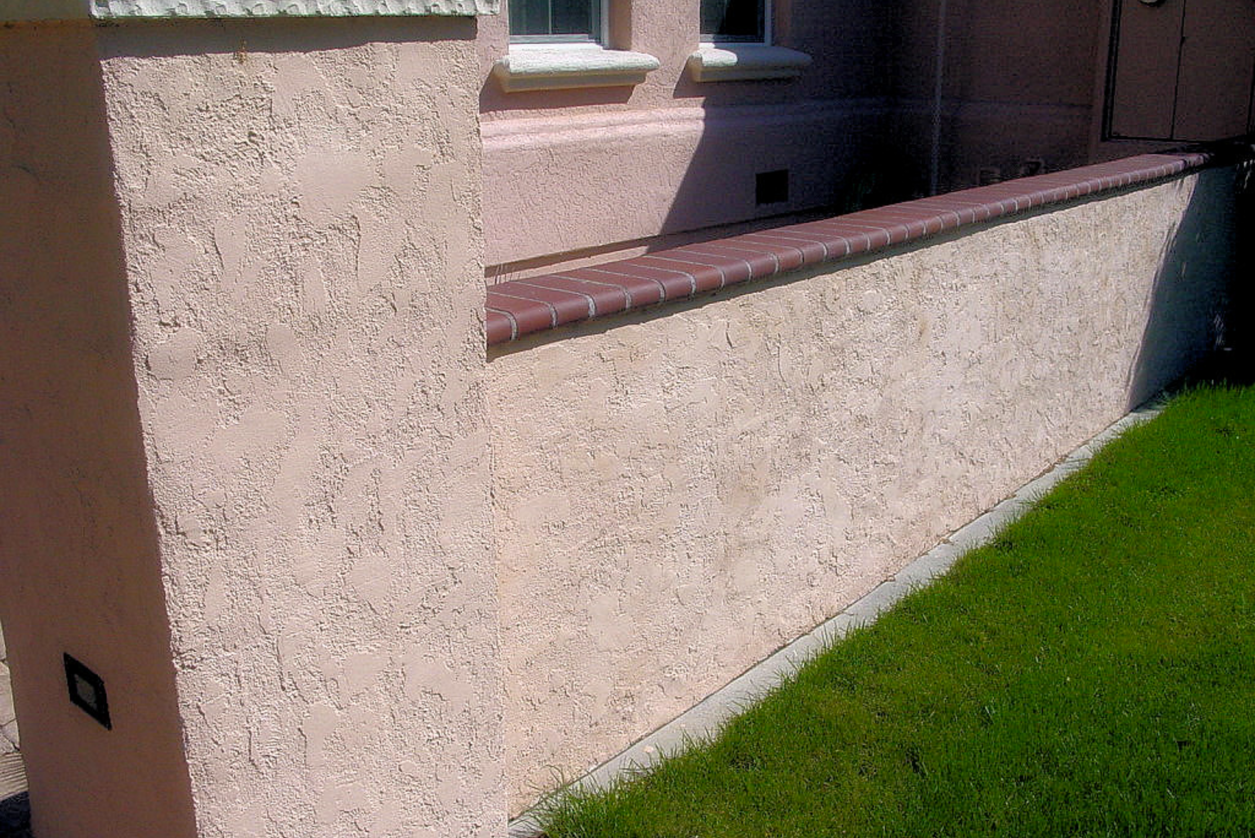 A pinkish concrete fence with stucco finish and brick cap top.