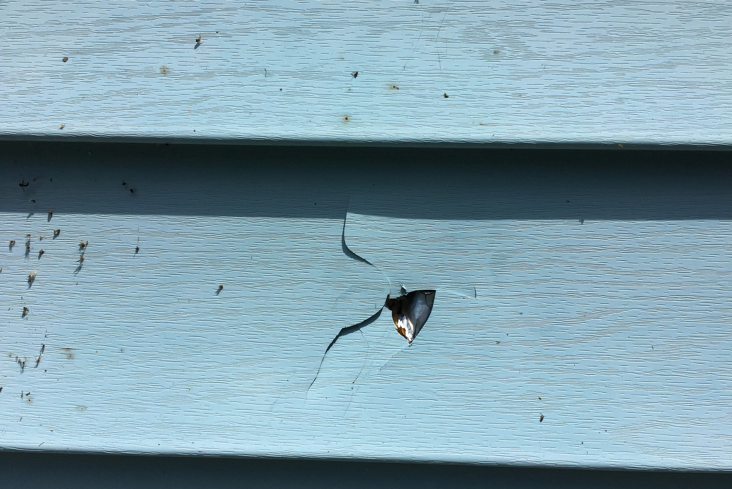 Blue vinyl siding with a hole and few cracks.