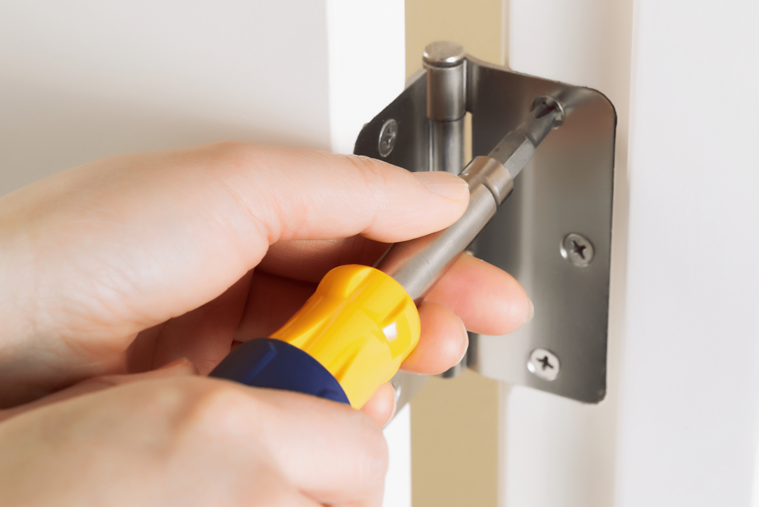 Closeup of someone's hands using a screw driver to tighten door hinge.