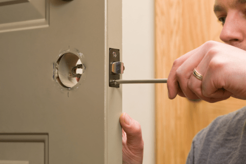 A door missing the handle with person using screw driver to assemble the door stricker.