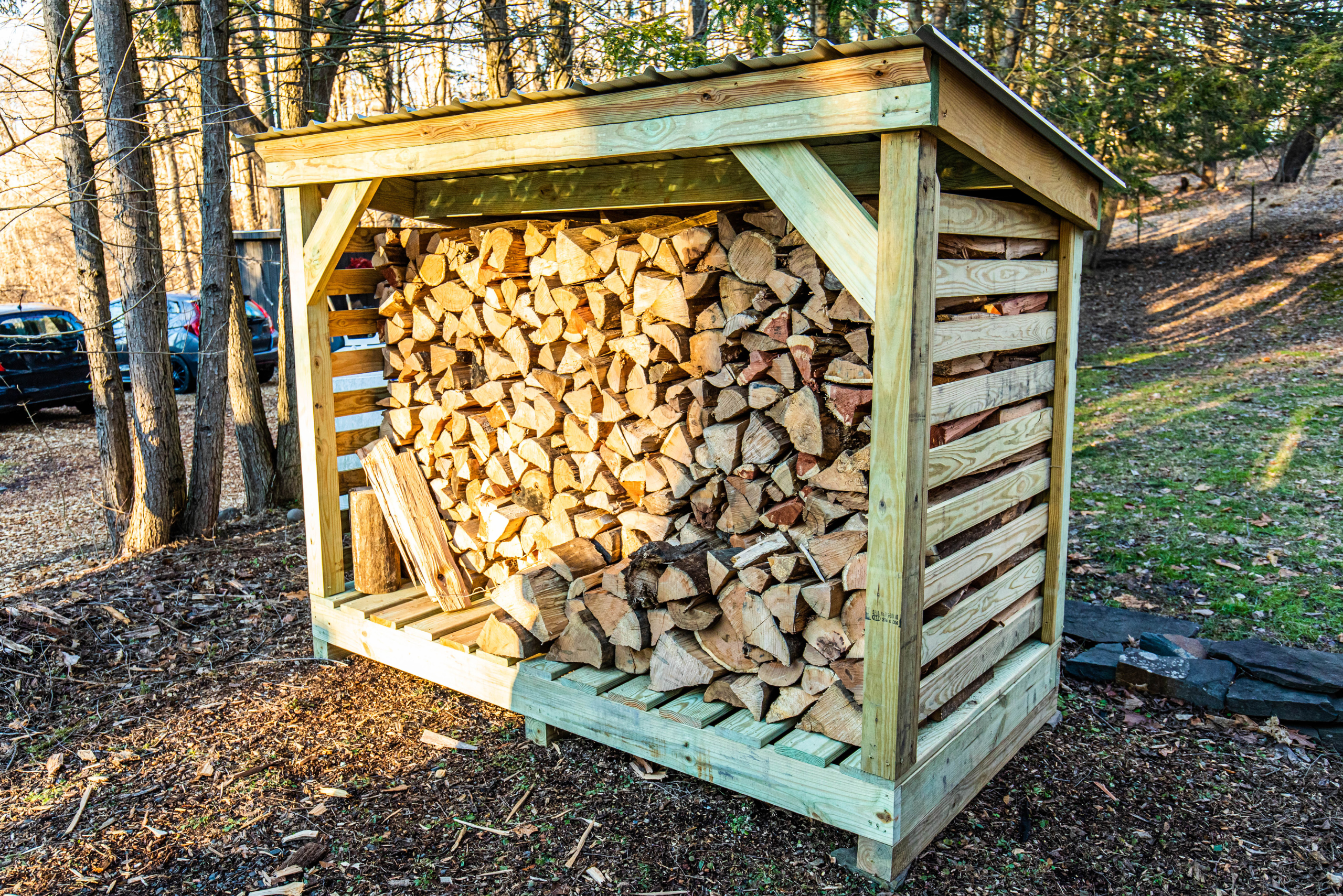 Large DIY firewood rack outdoors with shingled roof.