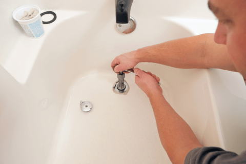 Person using special tool to tighten bathtub drain back on with paste.