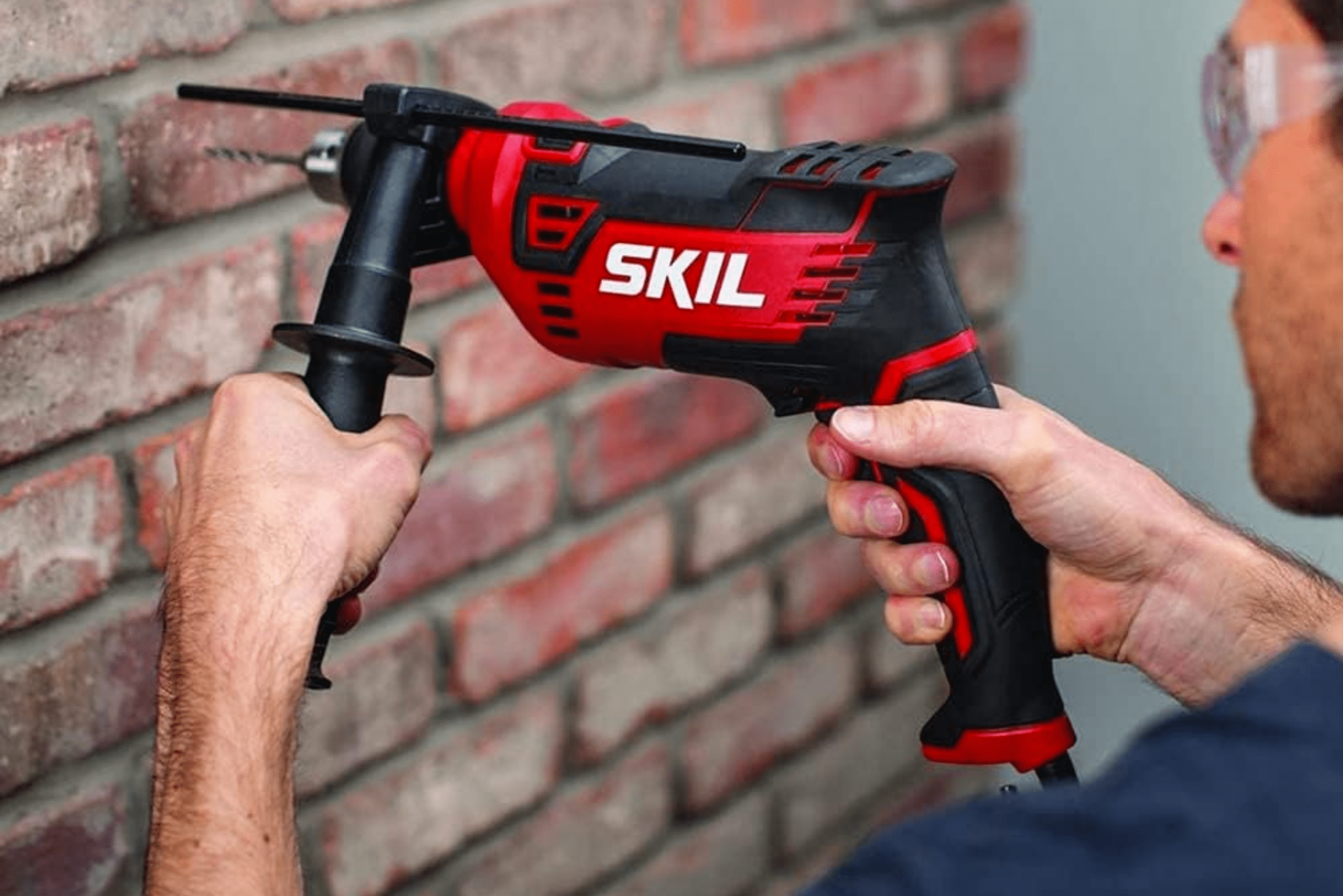 A Skil hammer drill being used on a red brick exterior wall.