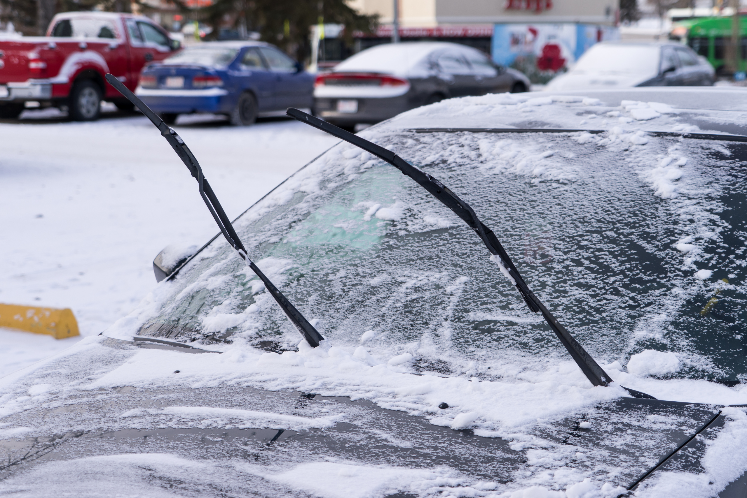 Car covered in snow and ice with its wiper blades lifted up while parked.