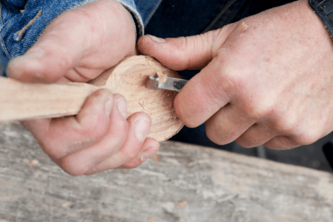 Closeup of someone's hands carving a wooden spoon.