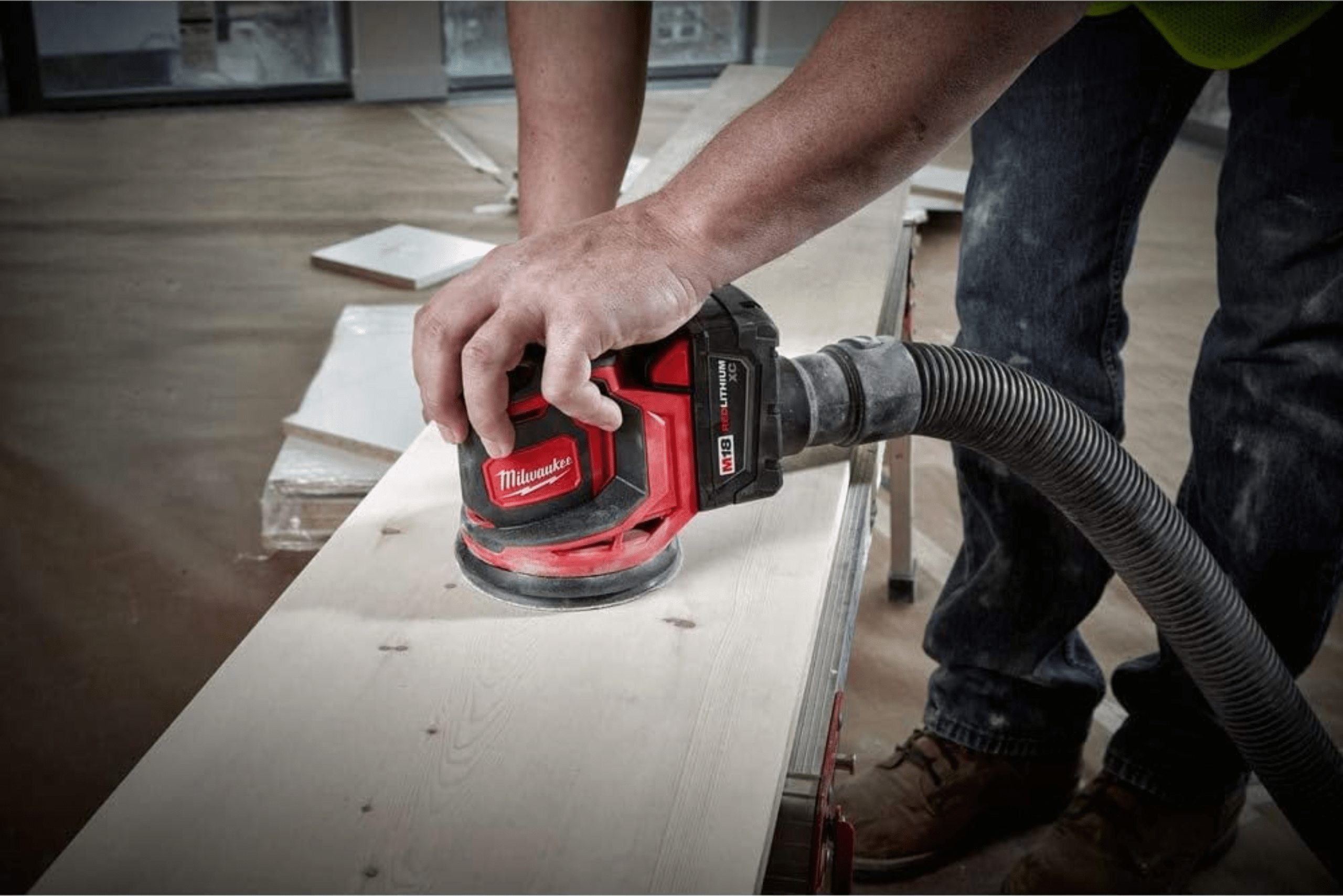 Milwaukee sander power tool attached to a dust hose being used to sand a wooden board.