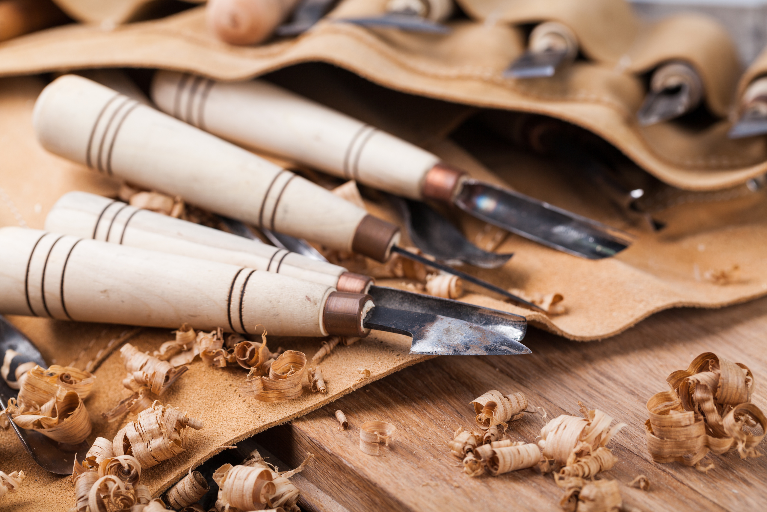 Carving tools and wood shavings on top of a leather carrying case.