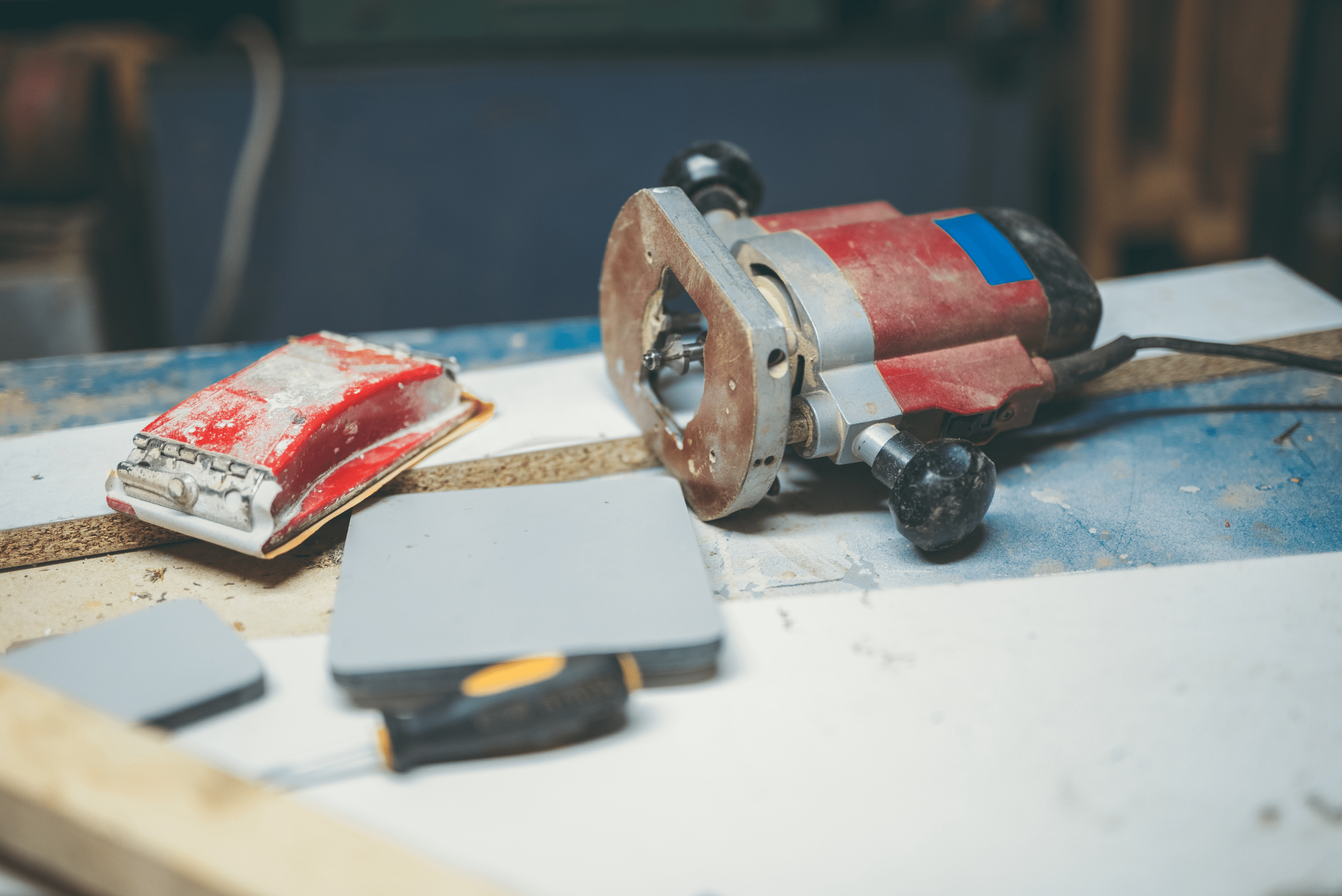 A router and sand block placed on top of wooden board.