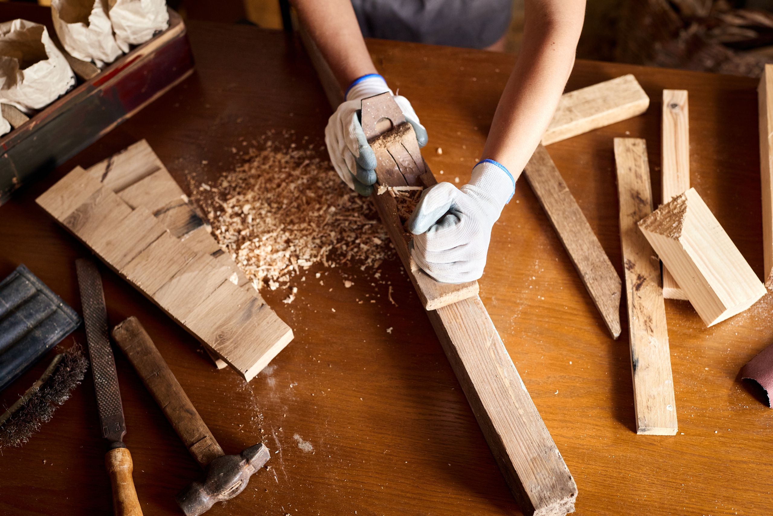 A top view of a wood workshop worker using a planer on the edge of a wood board.