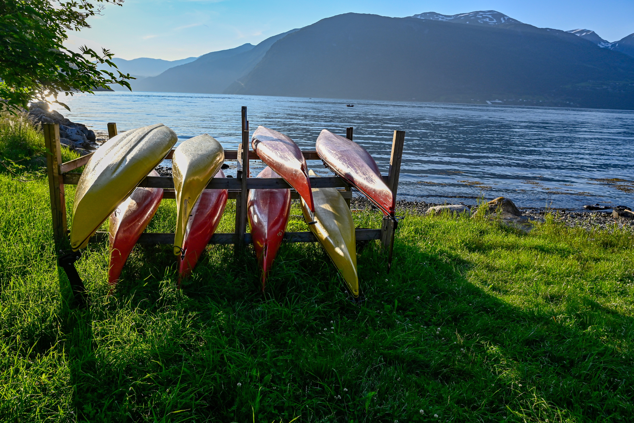 A DIY kayak rack on grass flanked by lake and mountain. 