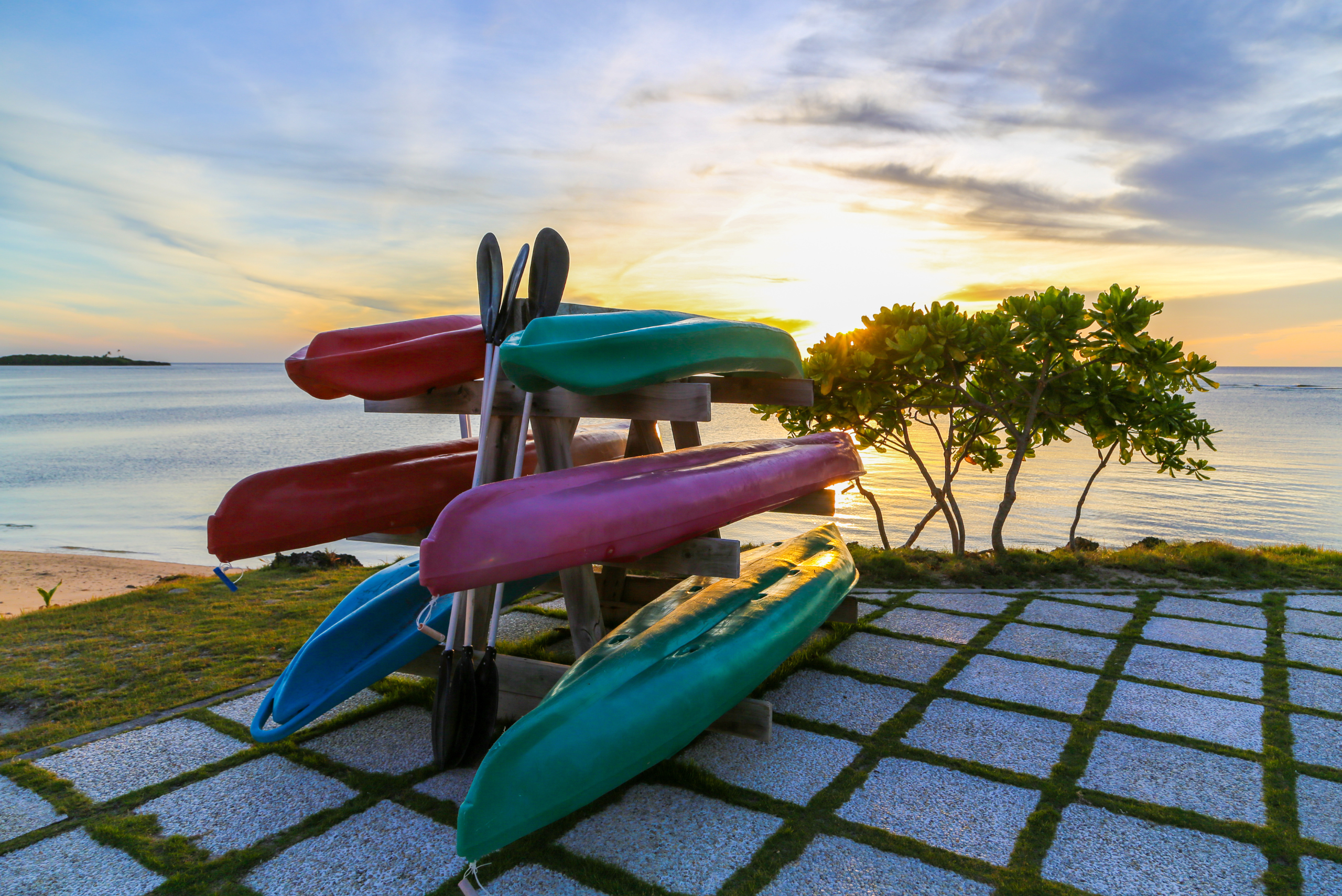 A DIY kayak rack on concrete platform with grass growing between the slaps.