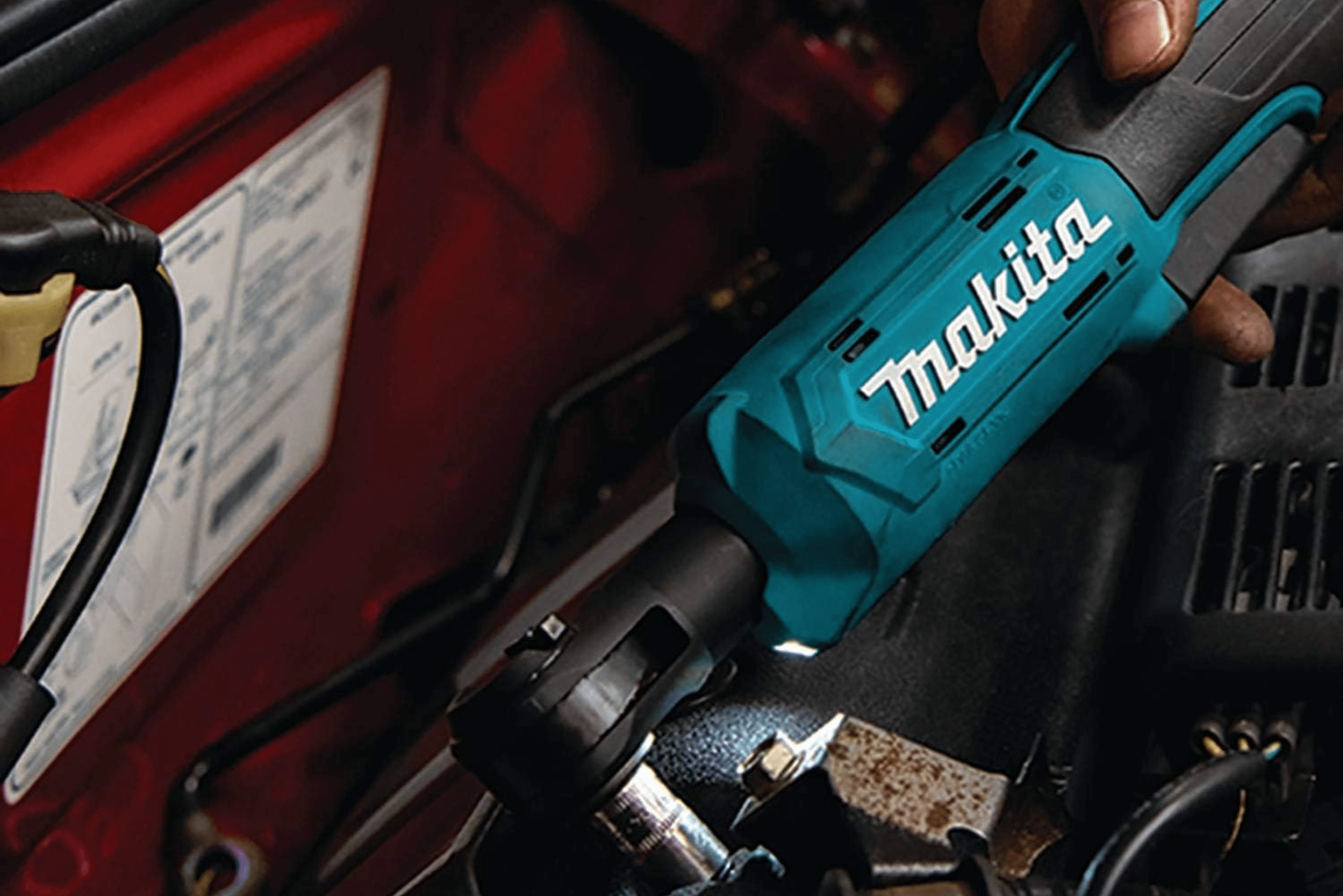 A closeup of a Makita ratchet wrench power tool taking off a bolt in an engine bay.