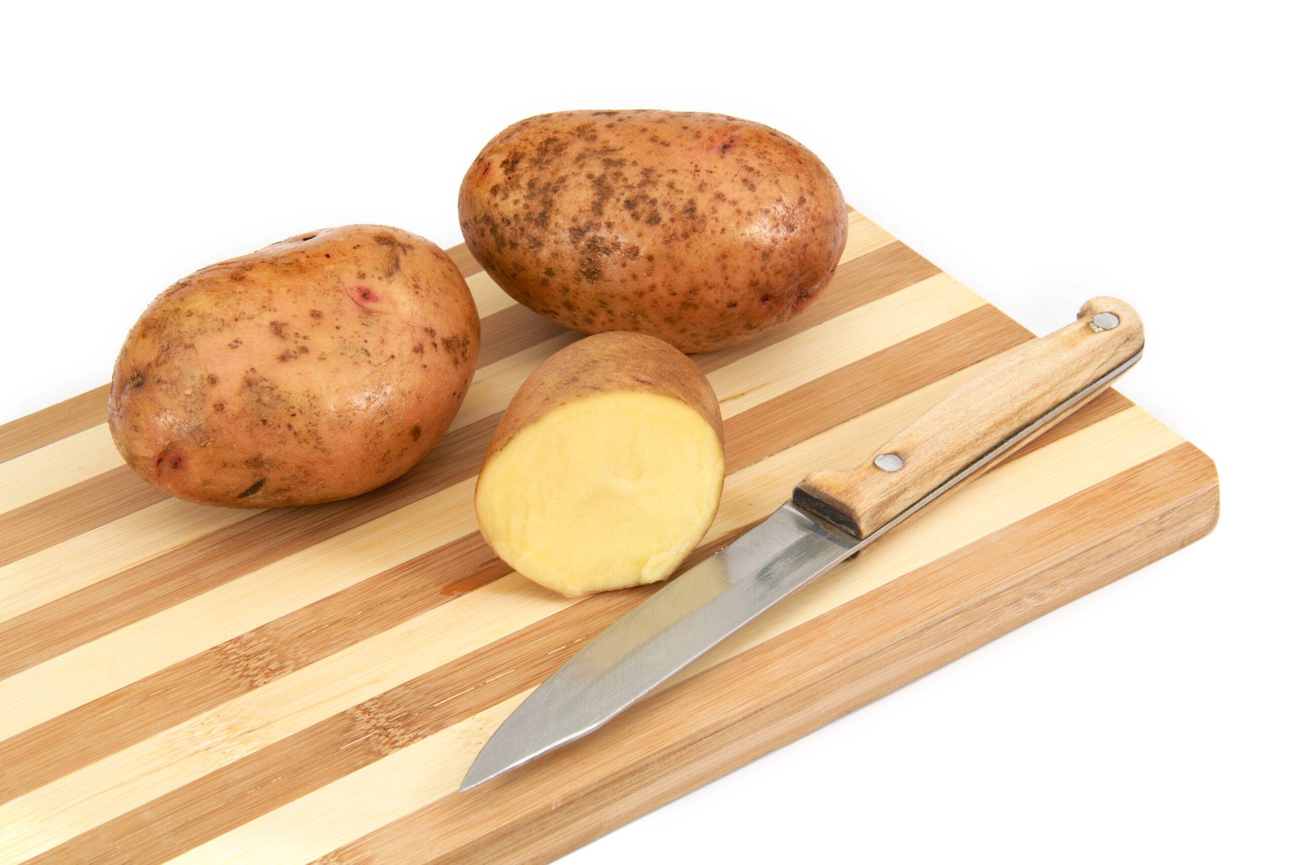 Raw potato tubers lying on a cutting board, isolated on a white background