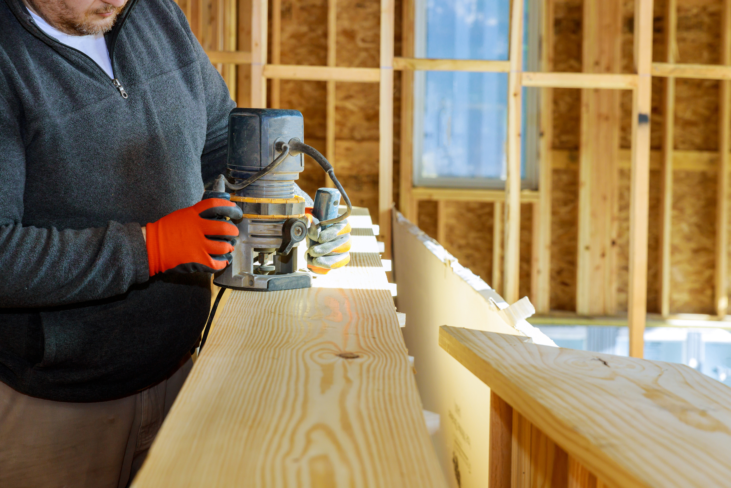 Closeup of someone's hands using a router on a piece of wood.