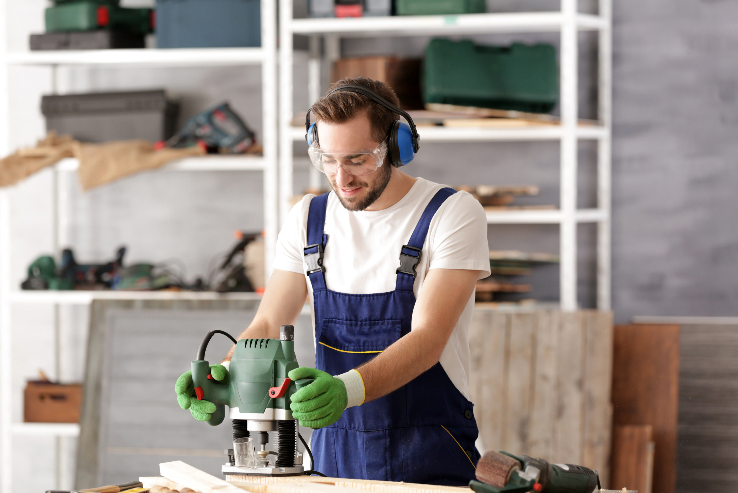 Man wearing protective equipment using a router on wooden board.