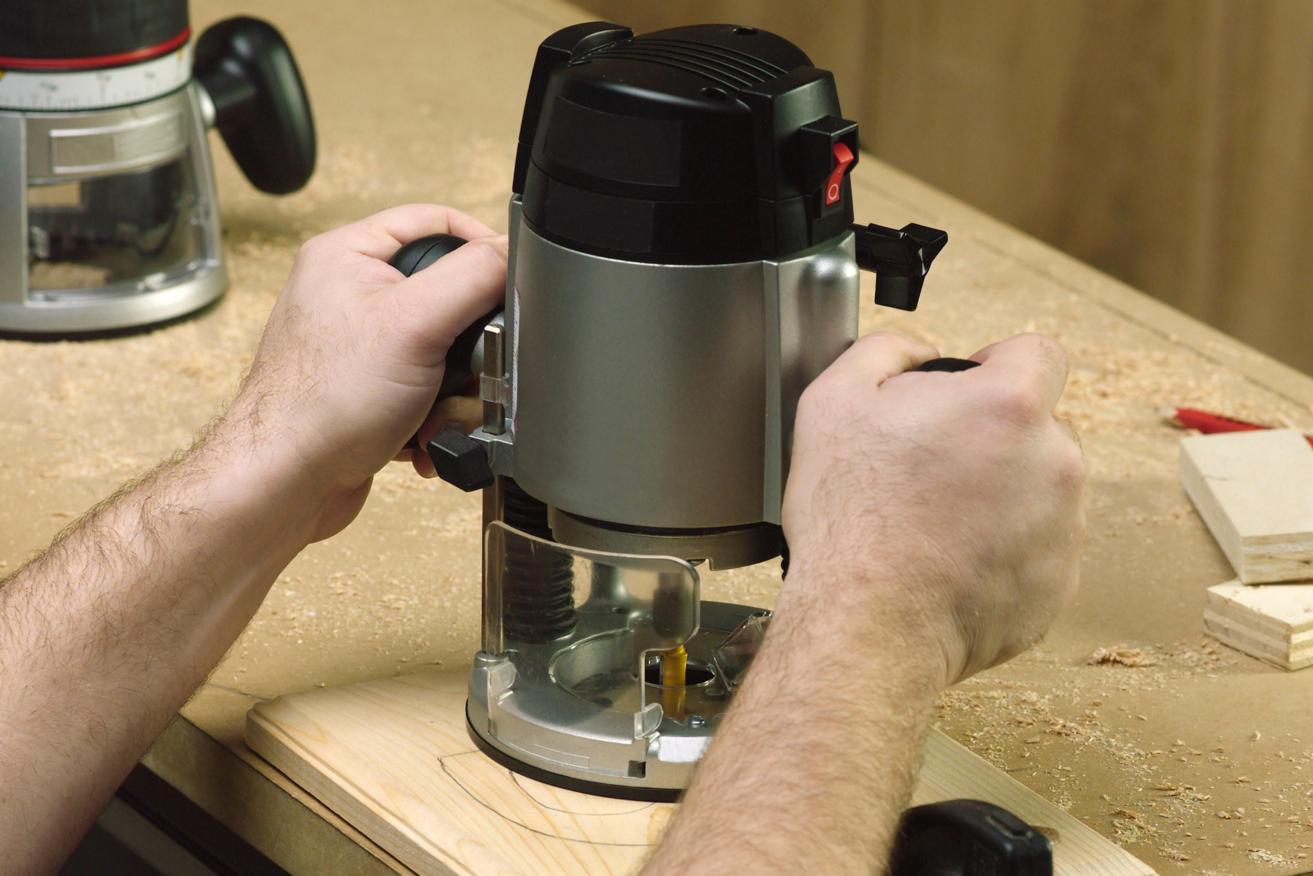 Two hands guiding a power router on wooden board.