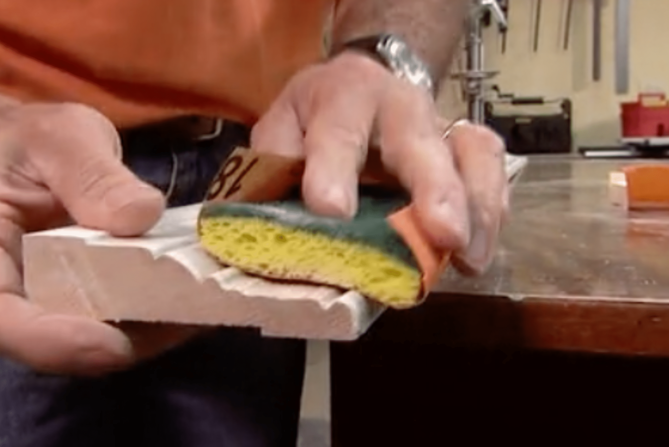 A closeup of someone's hands using a sponge with sandpaper wrapped around it.