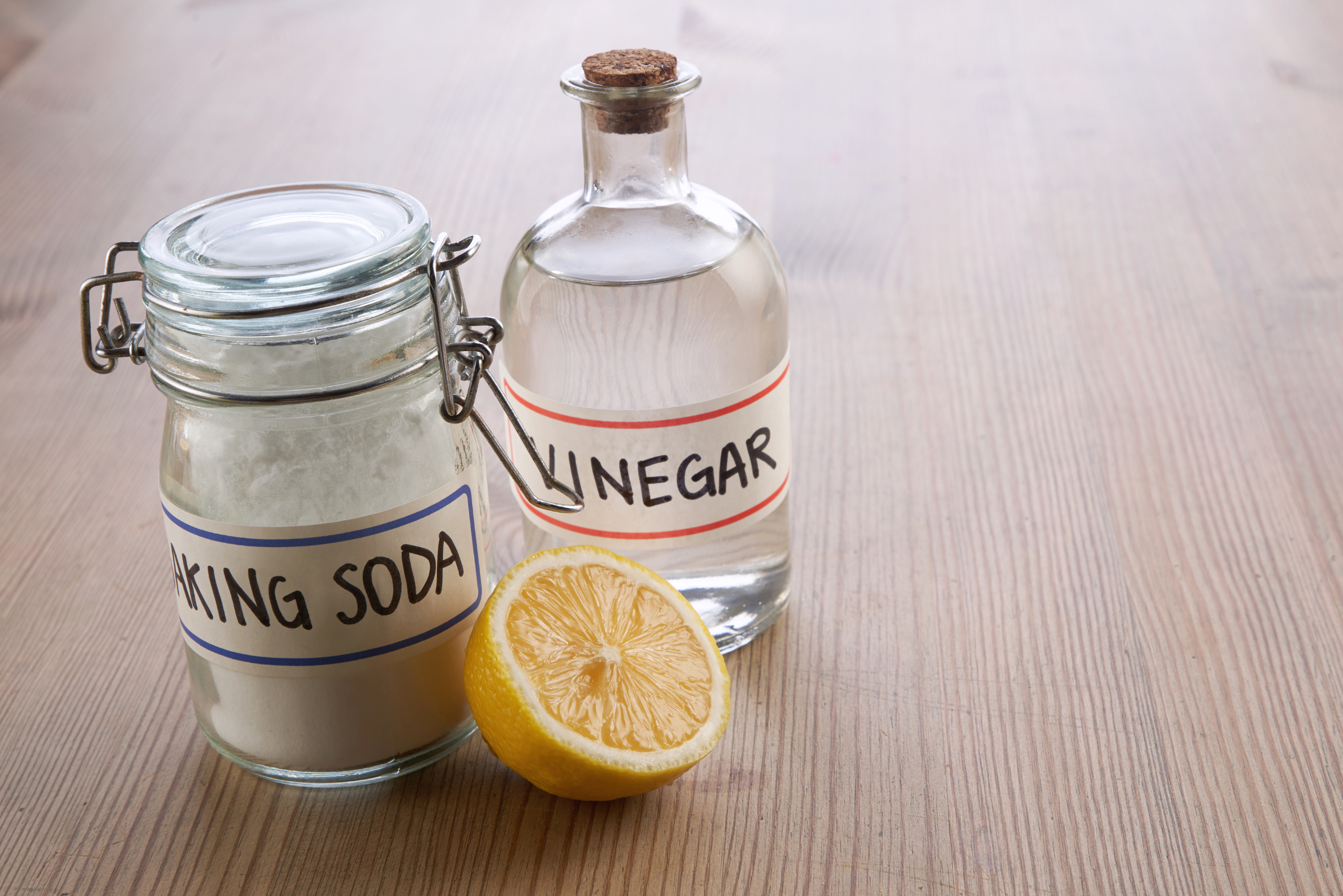 A jar of baking soda and bottle of vinegar behind half a lemon.