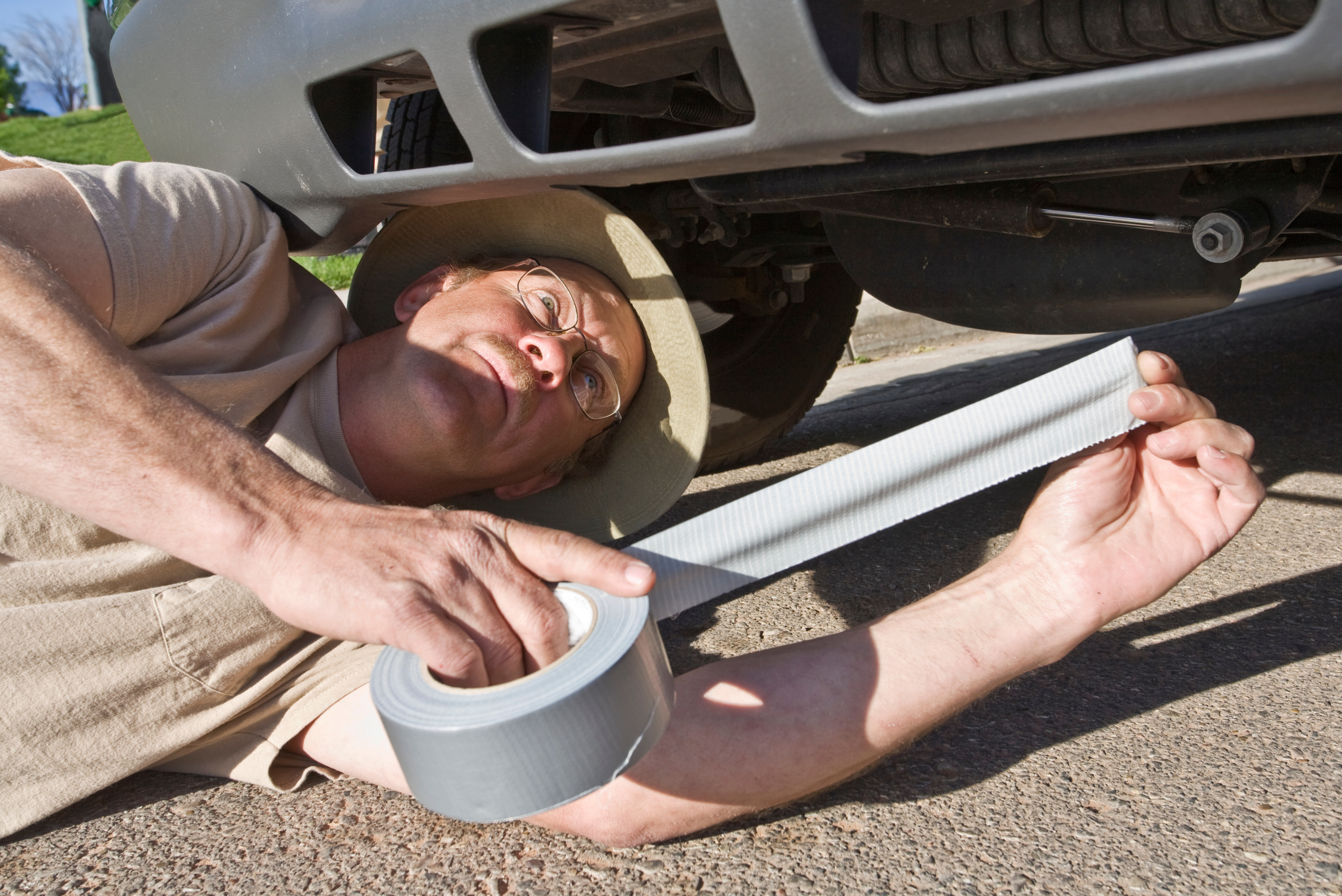 A man on the ground using duct tape to fix car bumper.