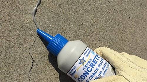 A closeup of someone's hand wearing a glove and using concrete filler to fix a hairline crack.