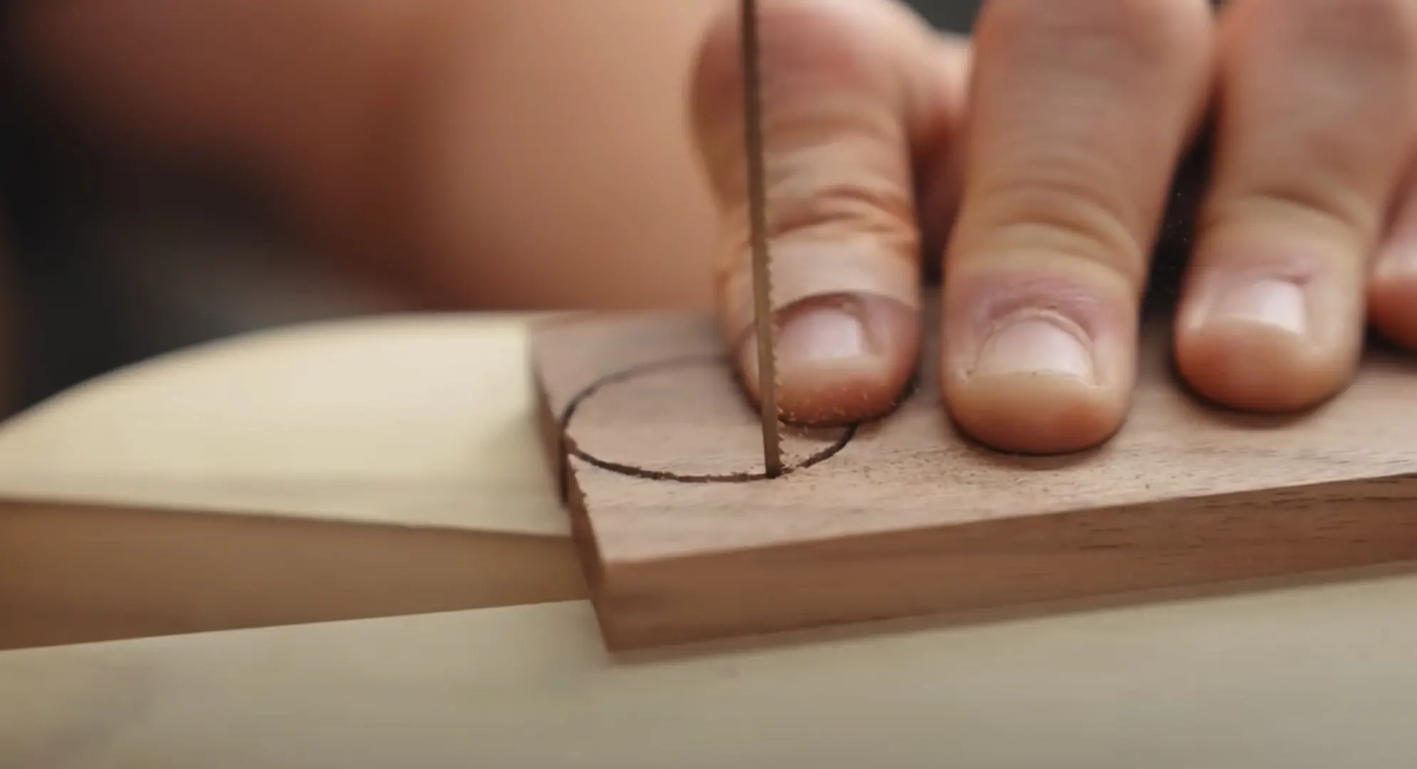 A closeup of coping saw and hand cutting a circle in wood.