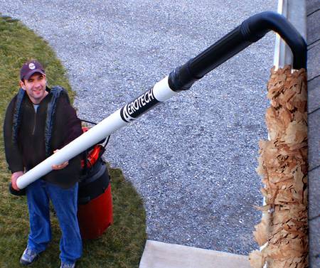 A person using an extension with a leaf blower to clean gutters without ladder.