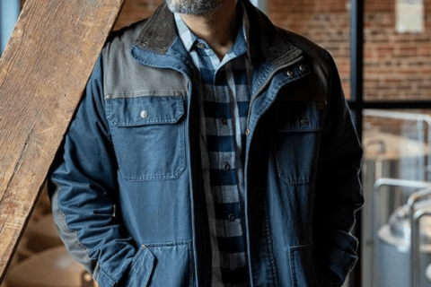 A man leaning on wooden beam while wearing a chore jacket.